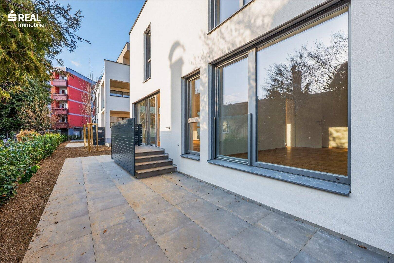 Geräumige Steinterrasse am Neubau mit großen Fensterfronten und Zugang zum Garten.