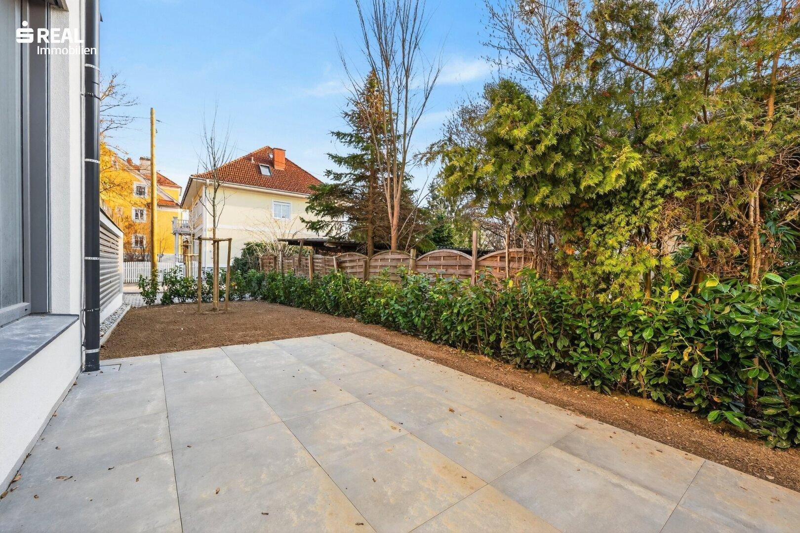 Sonniger Terrassenbereich mit Steinplatten und angrenzendem Garten, ideal zum Entspannen.