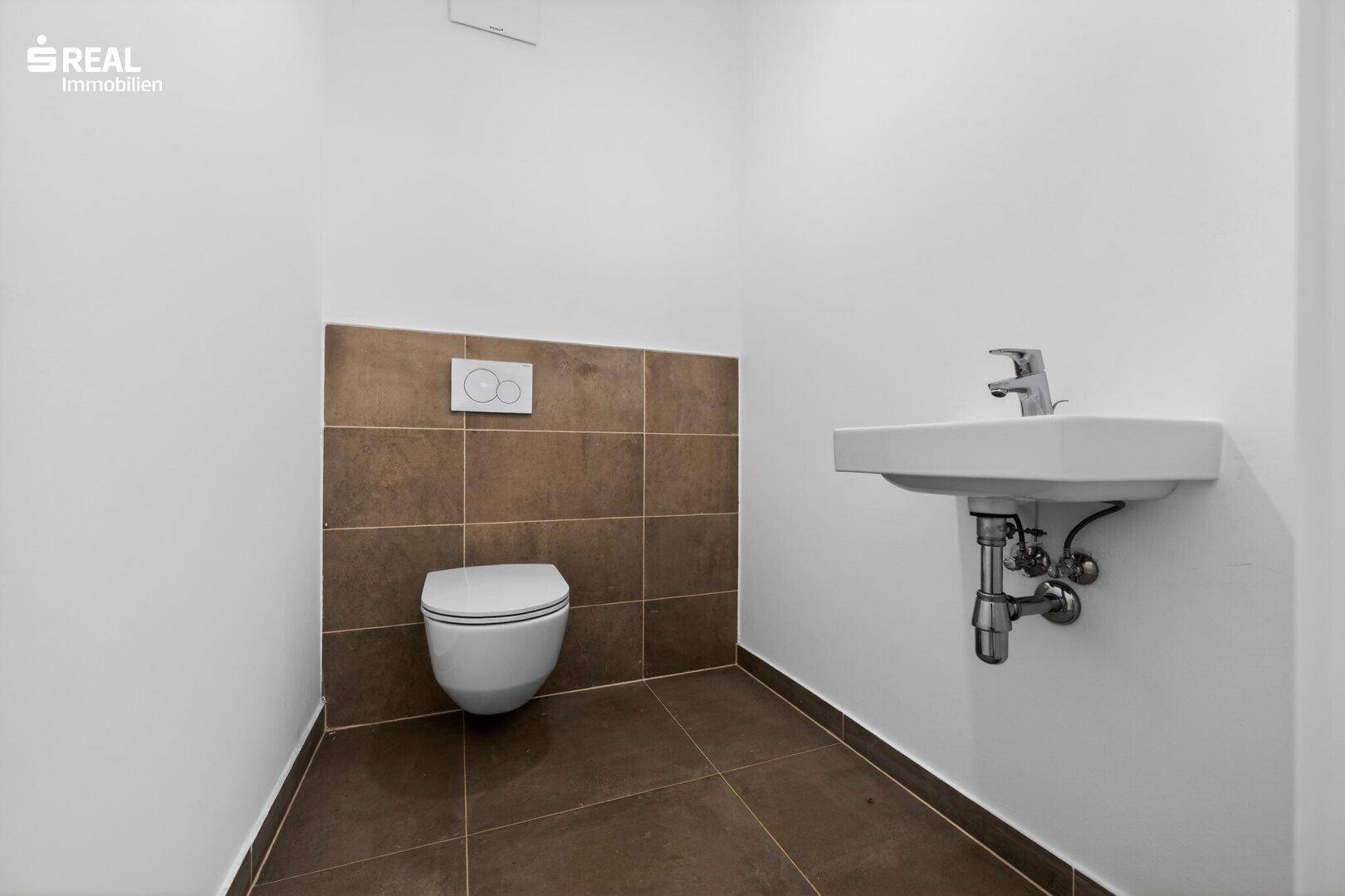 Separates Gäste-WC mit Wand-WC, Waschbecken und modernen braunen Fliesen.