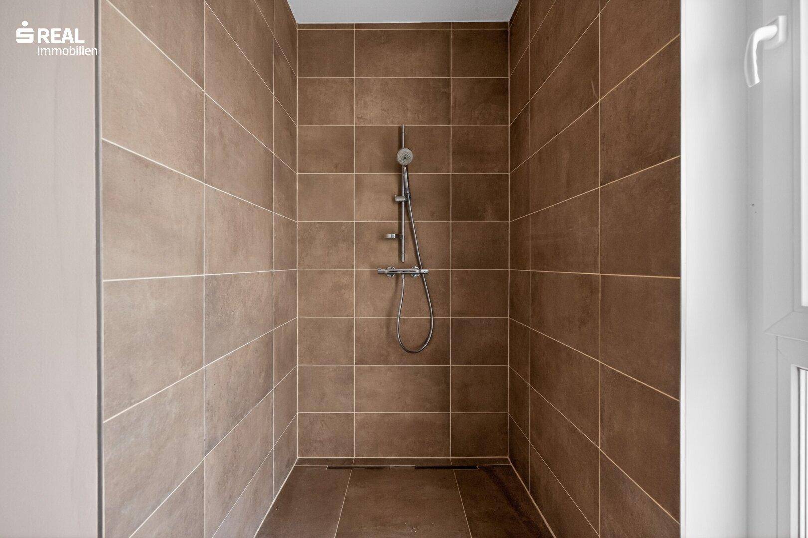 Moderne Duschkabine mit braunen Fliesen an Wänden und Boden, ausgestattet mit einer Regendusche.