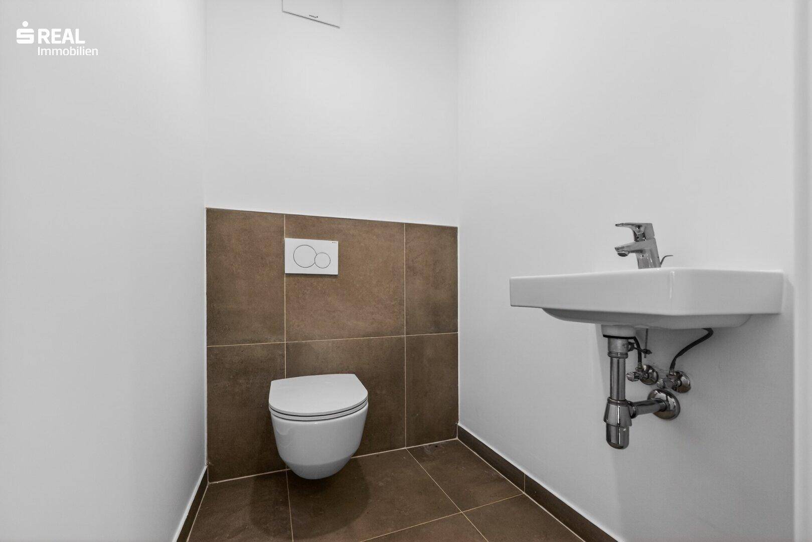 Modernes WC mit wandhängender Toilette und Waschbecken, ausgestattet mit braunen Akzentfliesen.
