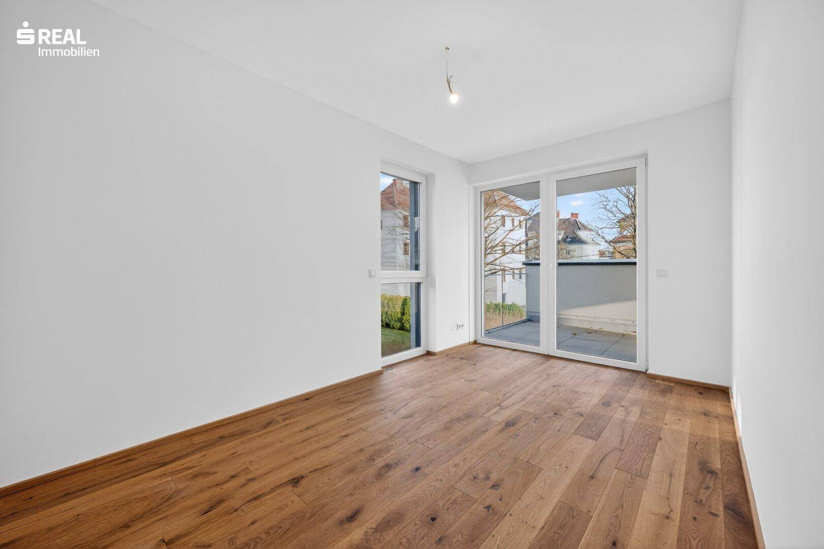 Helles Schlafzimmer mit Parkettboden und Zugang zu einem kleinen Balkon, bietet viel Tageslicht.