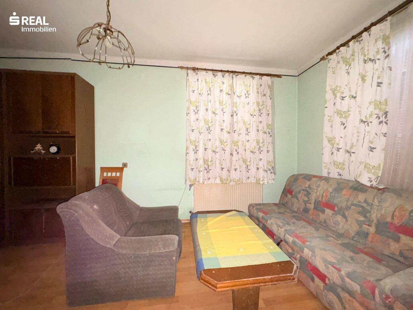 Wohnzimmer mit bequemen Sofas, floralen Vorhängen und einem Holzboden.