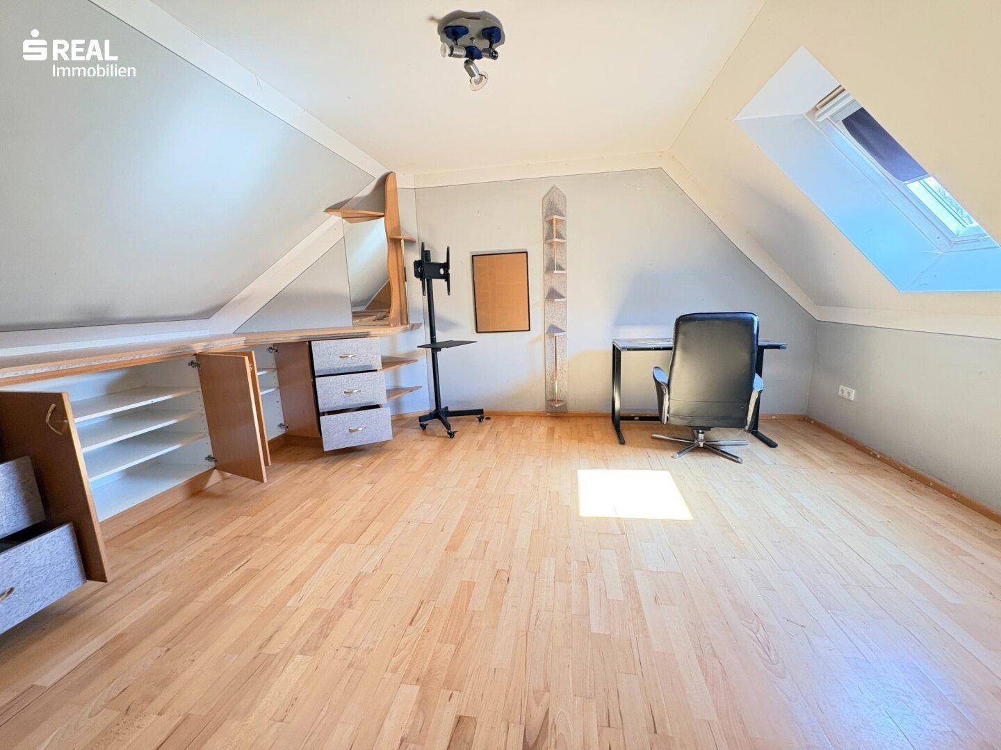 Helles Dachzimmer als Arbeitsbereich mit Schreibtisch, Dachfenster und Holzfußboden.