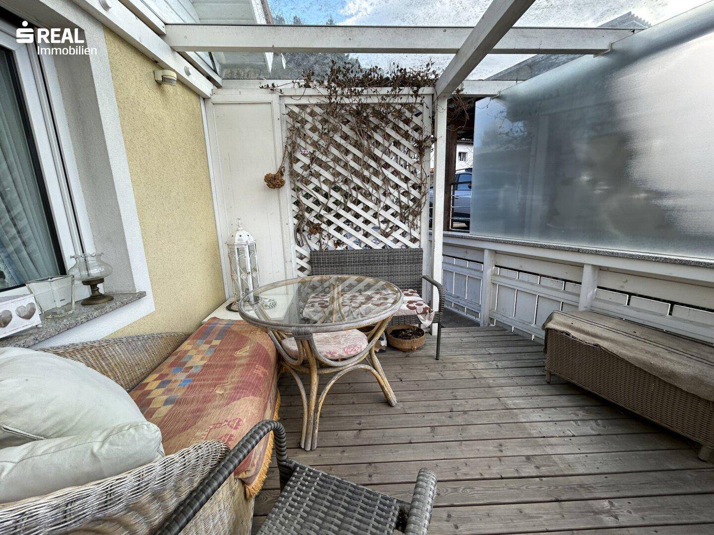 Überdachter Balkon mit Holzdeck und gemütlicher Sitzecke.