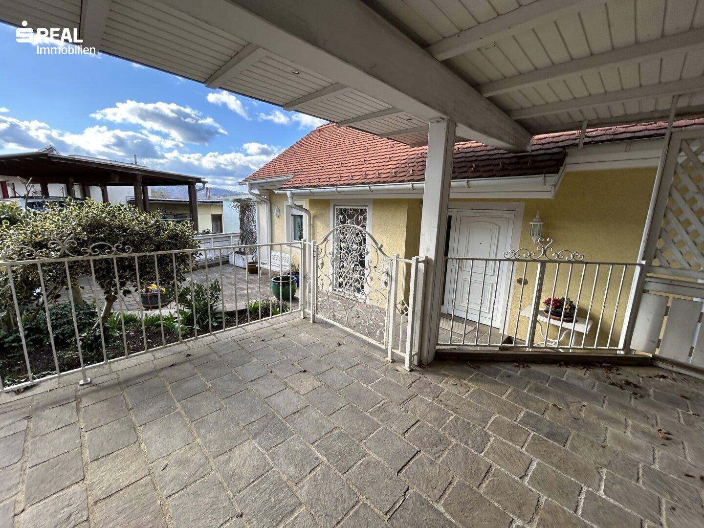 Überdachte Terrasse mit Steinboden und schmiedeeisernem Geländer.