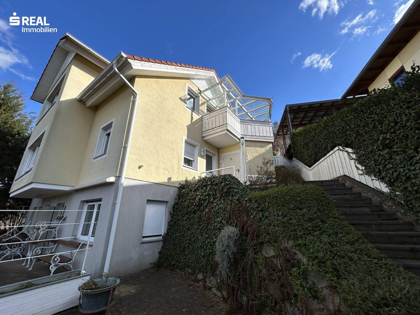 Ansicht des Hauses mit einer gepflasterten Terrasse und einer Treppe zum Garten.