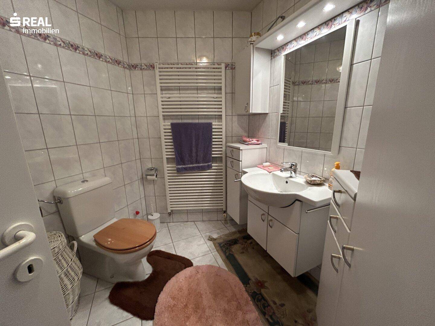 Badezimmer mit Waschbecken, WC, beheiztem Handtuchhalter und weißen Fliesen.