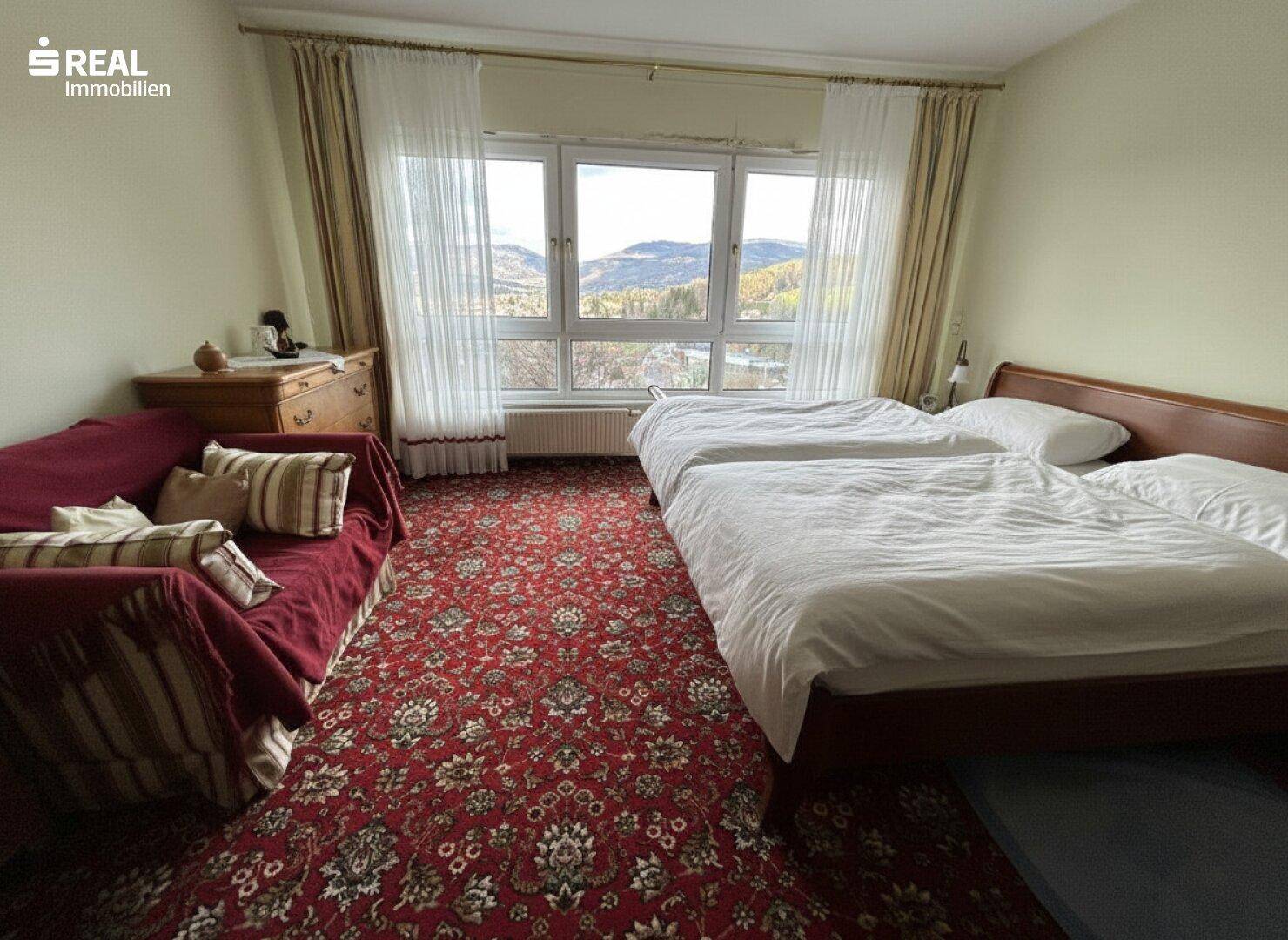 Schlafzimmer mit Teppichboden, zwei Betten und weitem Blick auf die Berge.