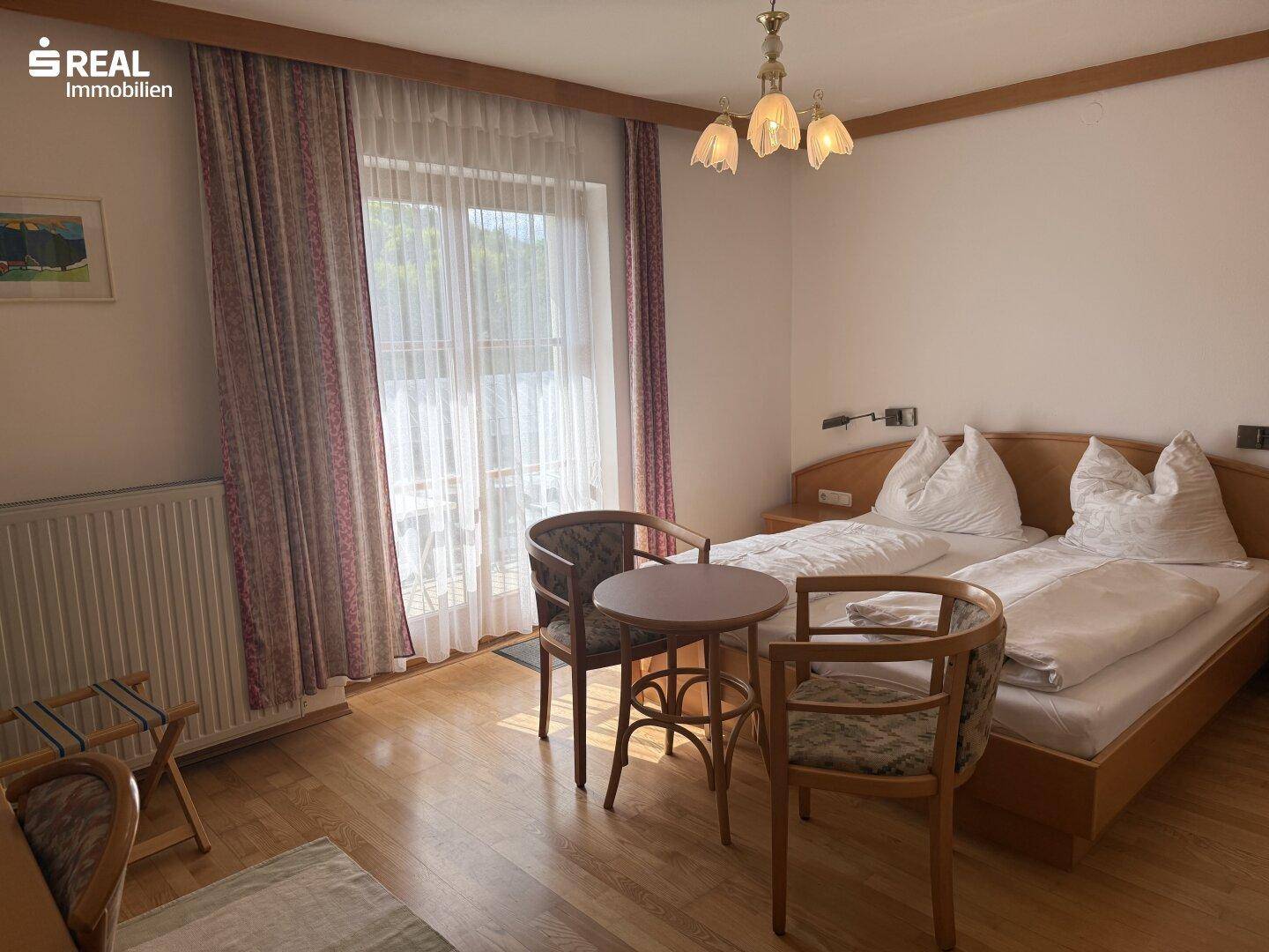 Gemütliches Schlafzimmer mit zwei Einzelbetten, Holzboden und Vorhängen vor einem großen Fenster.
