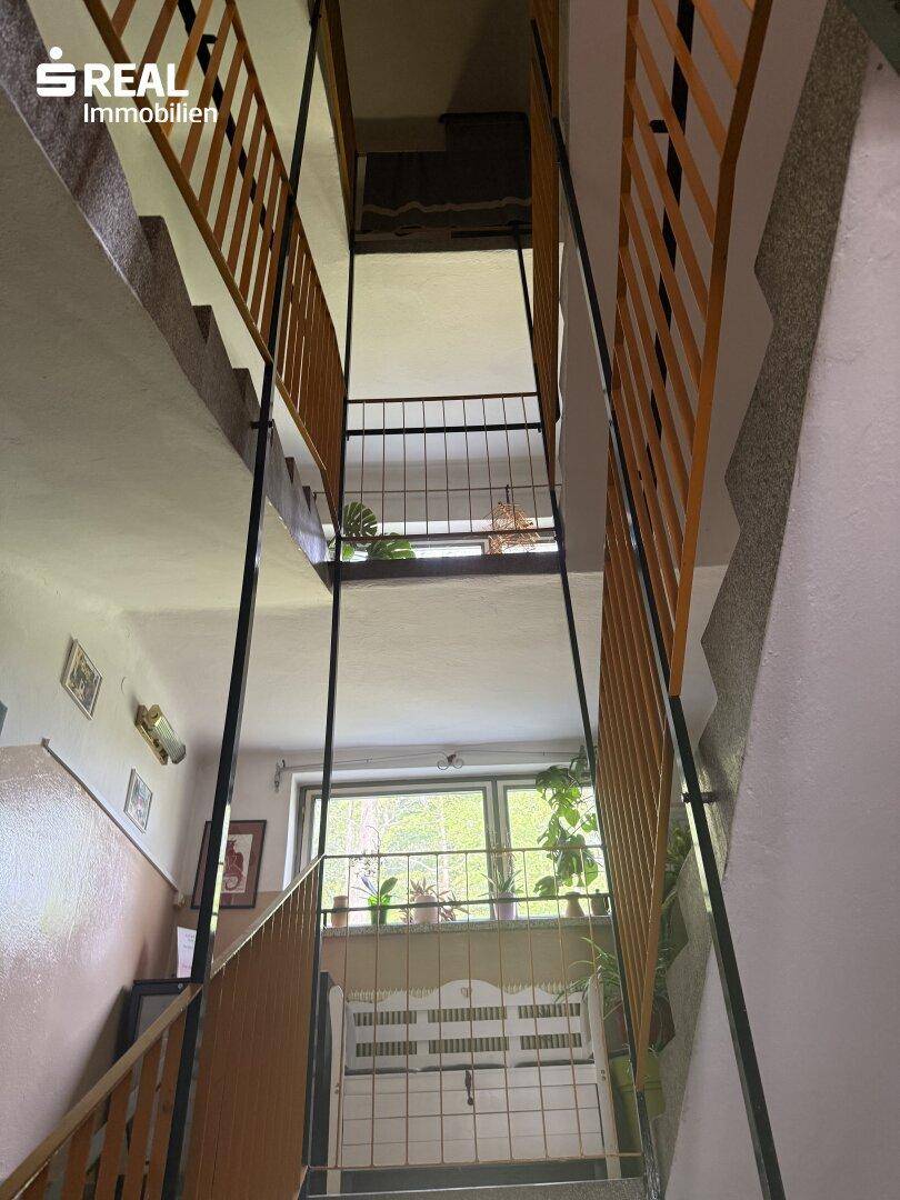 Geräumiges Treppenhaus mit mehreren Etagen, Holzgeländer und einem Fenster, das Tageslicht hereinlässt.