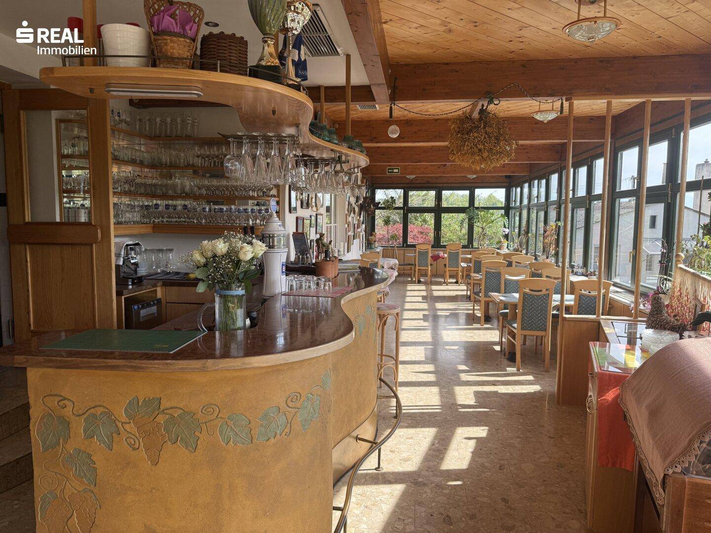 Gemütlicher Restaurantbereich mit einer rustikalen Bar, Holzbalkendecke und vielen Fenstern.