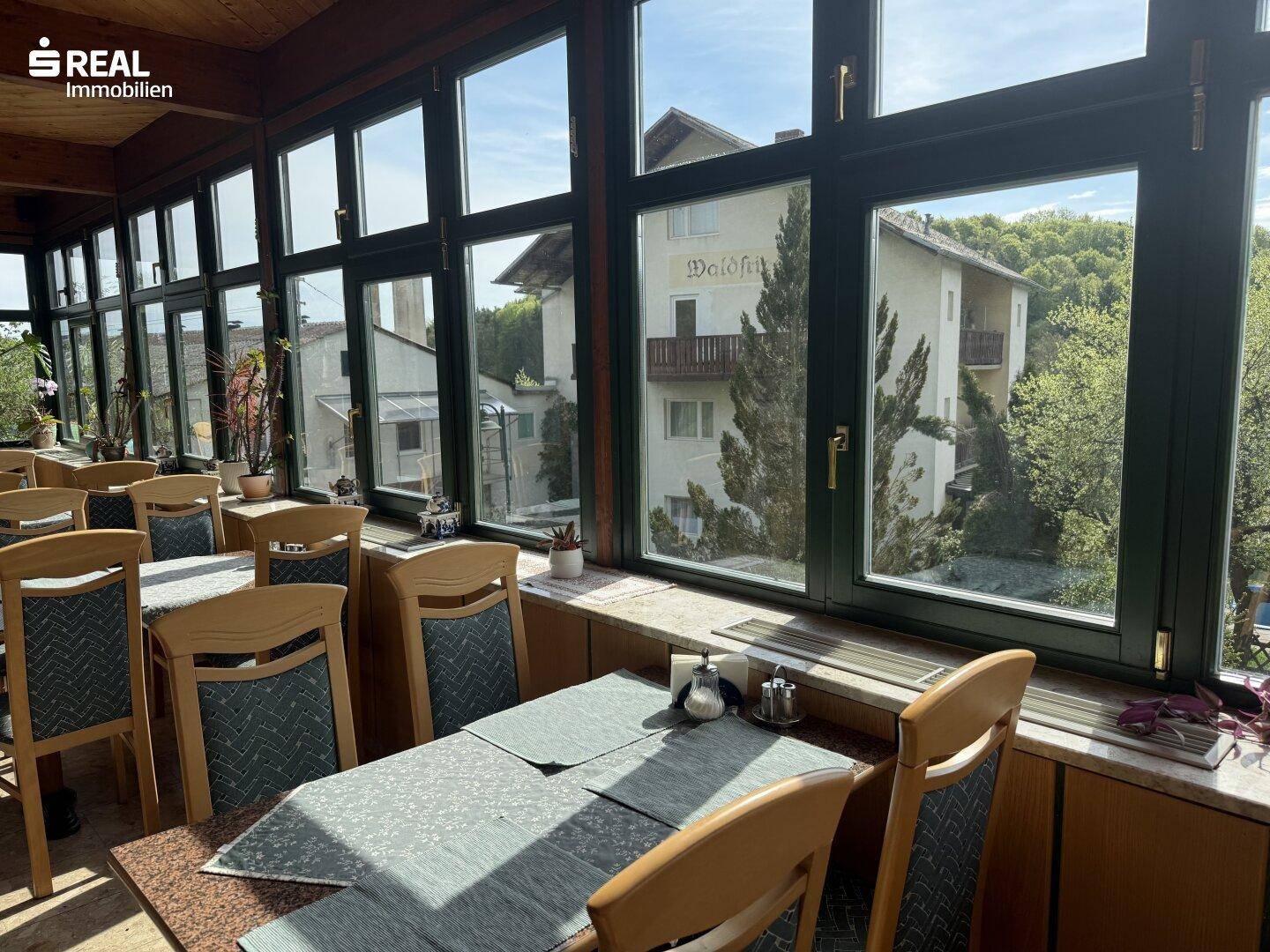 Essbereich eines Restaurants mit großen Fenstern, die einen Blick auf ein benachbartes Gebäude und die Umgebung bieten.