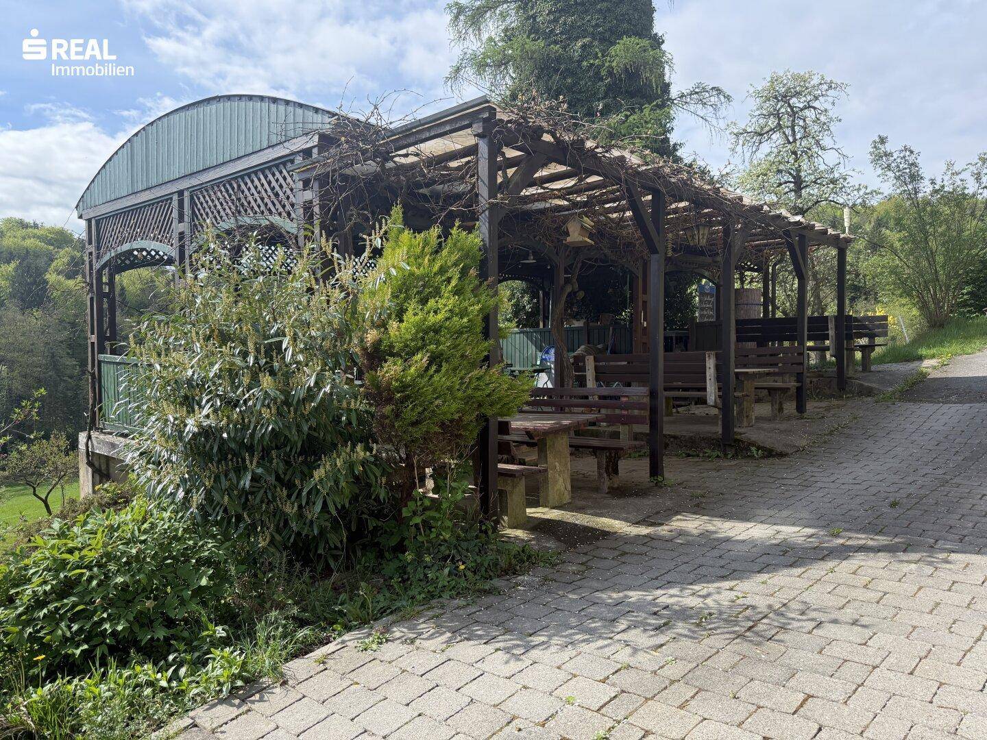 Überdachter Außenbereich mit Holzbänken und Tischen, ideal für Mahlzeiten im Freien in natürlicher Umgebung.