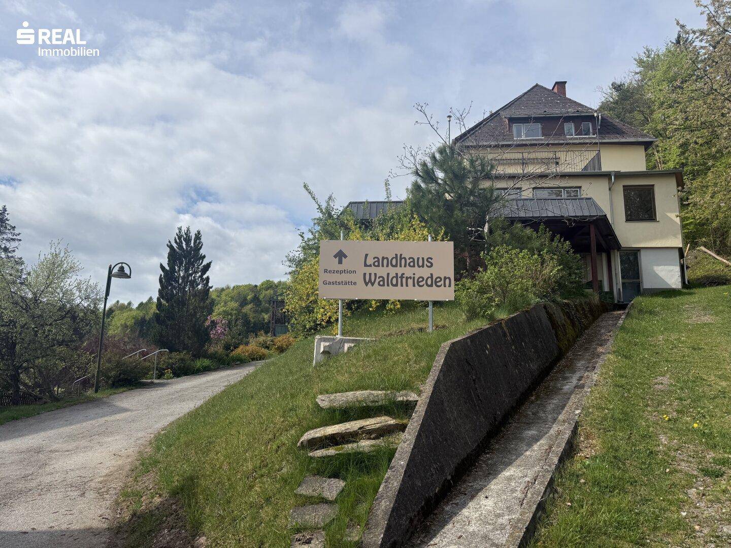 Zufahrt zu einem Landhaus mit einem Wegweiser, der zur Rezeption und Gaststätte "Waldfrieden" führt.