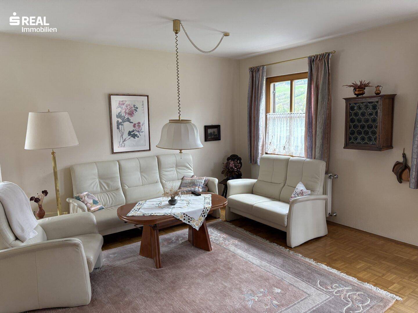 Helles Wohnzimmer mit bequemen Sofas, Parkettboden und traditionellem Teppich.