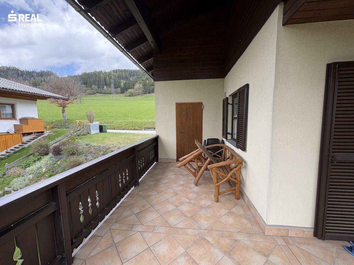 Überdachter Balkon mit Fliesenboden und Blick auf die umliegende Natur und Landschaft.