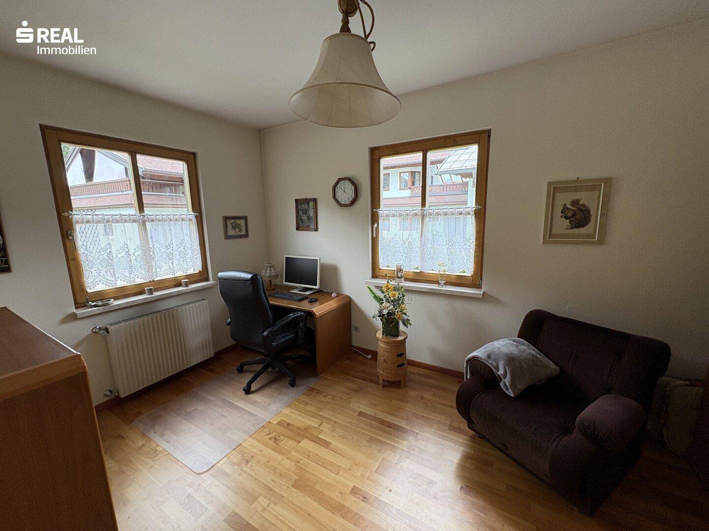 Helles Arbeitszimmer mit Holzparkett, Schreibtisch und Blick ins Grüne.
