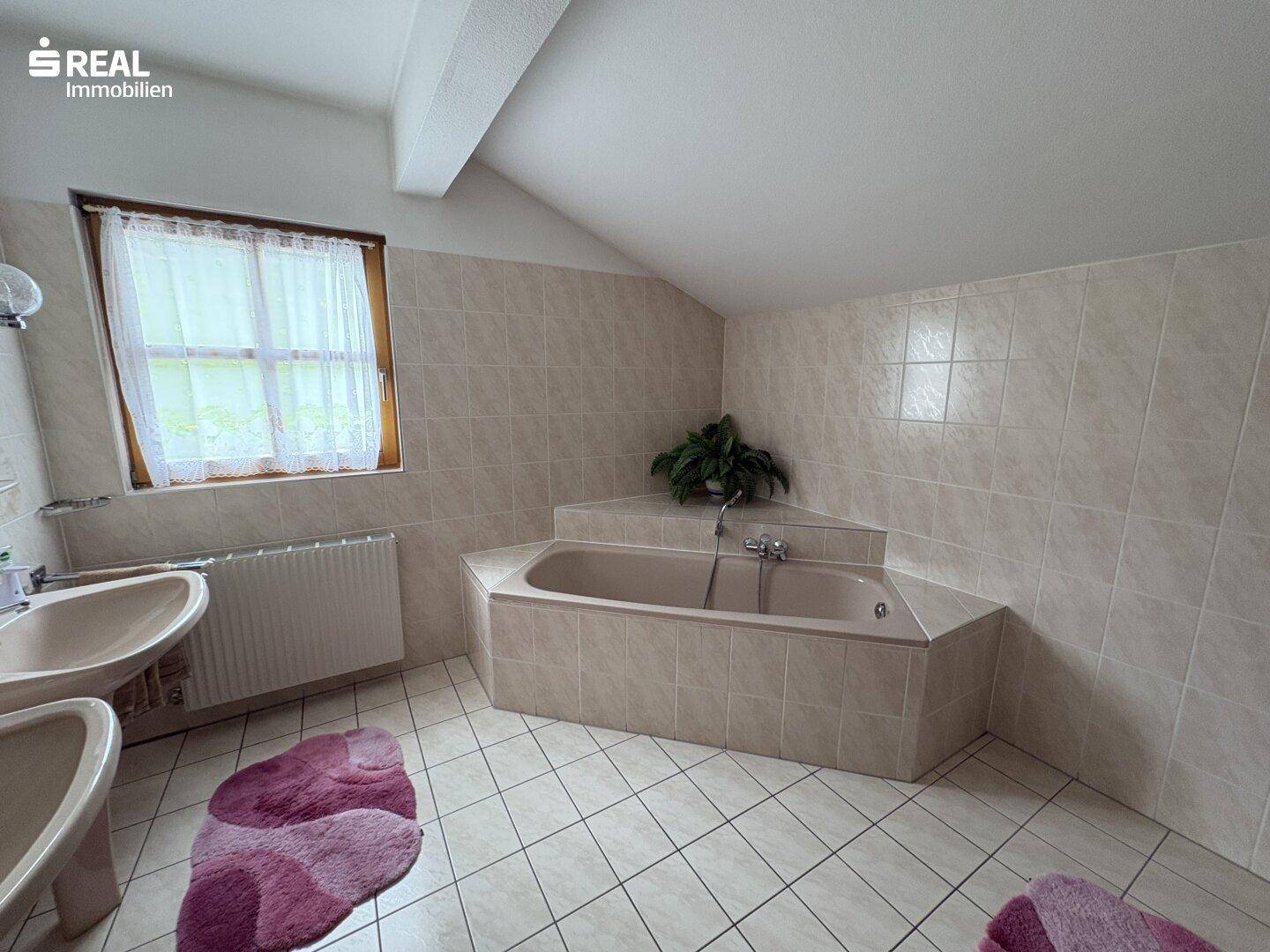 Badezimmer mit beigefarbenen Fliesen, Eckbadewanne und Fenster.