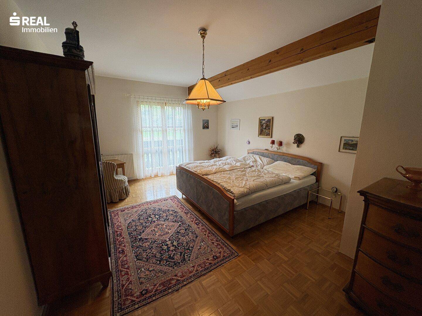 Helles Schlafzimmer mit Parkettboden, Holzbalken und Zugang zum Balkon.