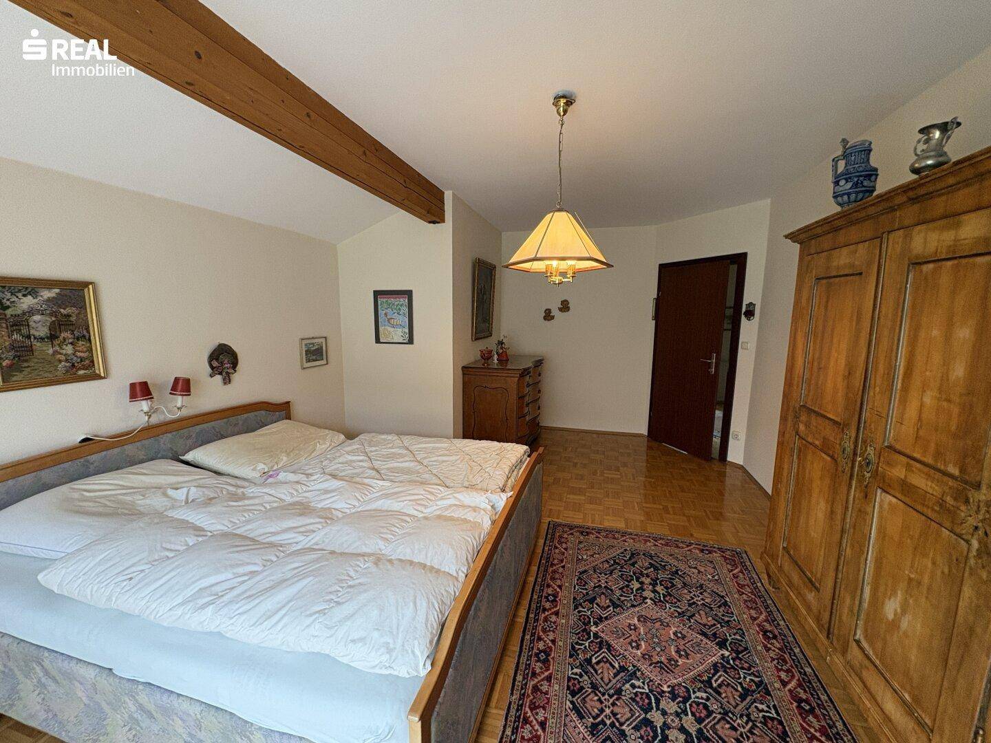 Geräumiges Schlafzimmer mit Parkettboden, Holzbalken und traditionellen Möbeln.