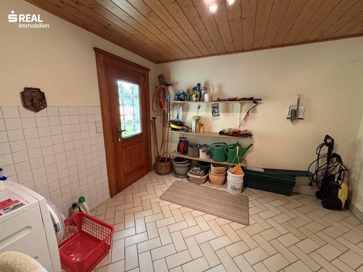 Praktischer Hauswirtschaftsraum mit Fliesenboden, Regalen und Waschmaschine.