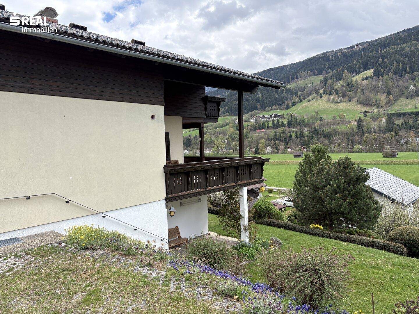 Seitenansicht des Hauses mit Balkon und weitem Blick über die grüne Landschaft und Berge.