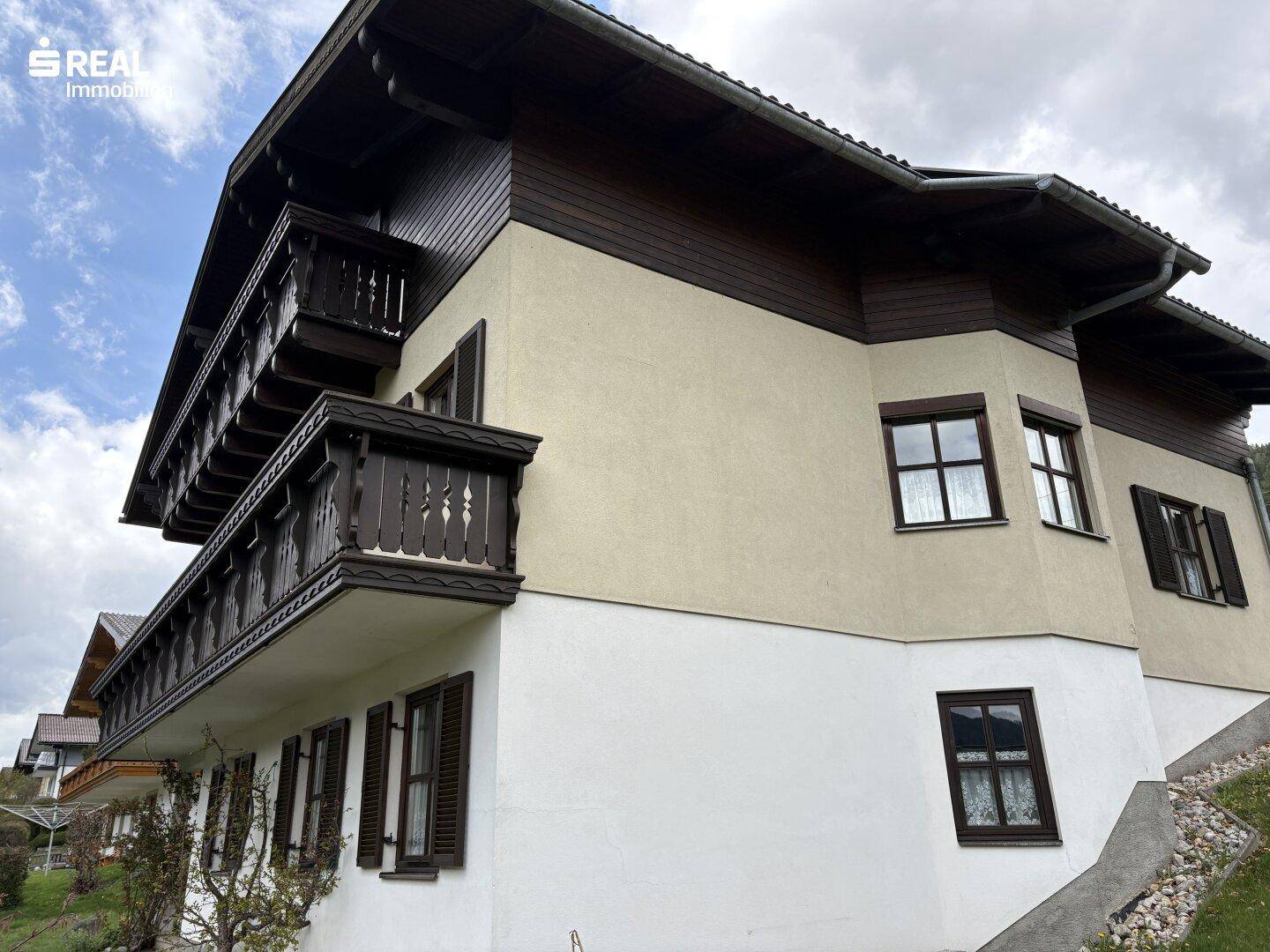 Fassade des Hauses mit traditionellen Holzfensterläden und Balkonen in ländlicher Umgebung.