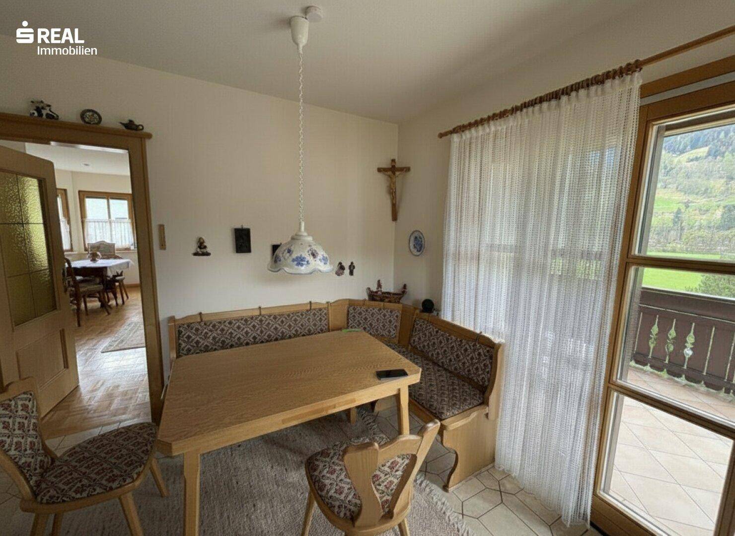 Gemütlicher Essbereich mit Eckbank, Holztisch und Blick ins Grüne durch das Fenster.