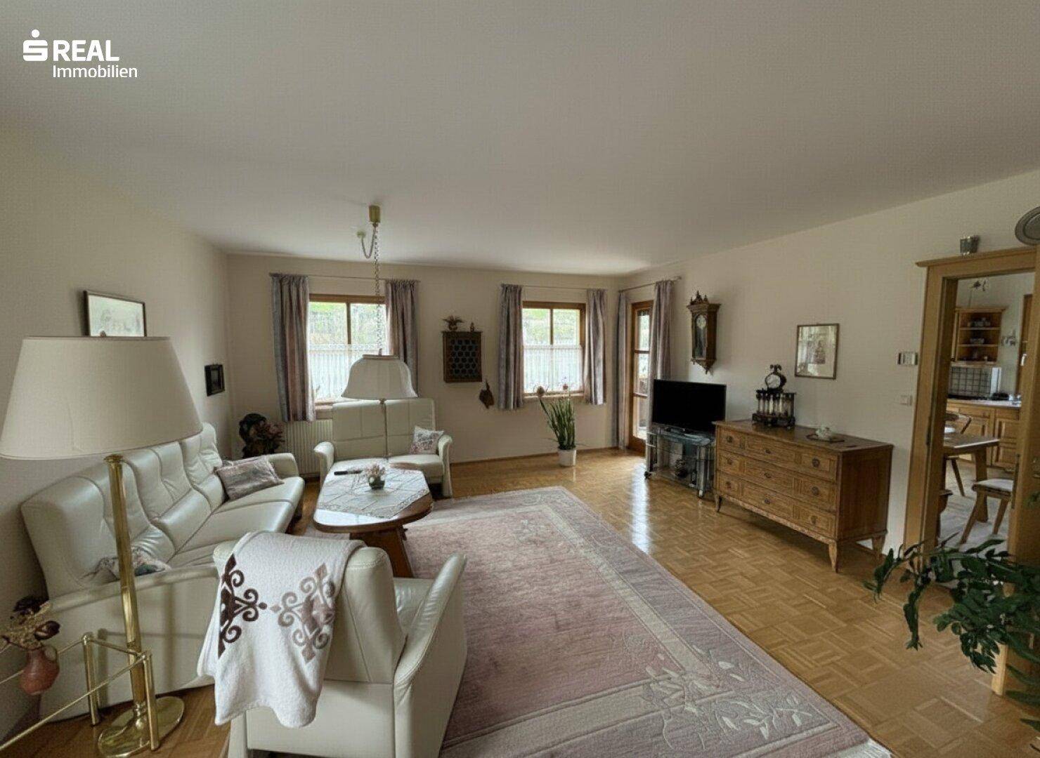 Geräumiges Wohnzimmer mit Parkettboden, Sitzgelegenheiten und Zugang zum Balkon.