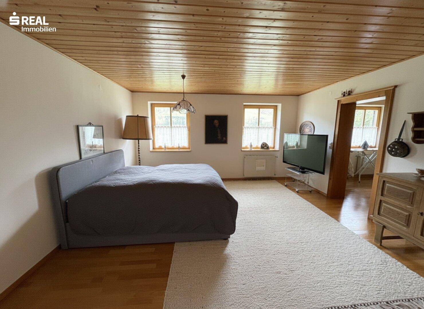 Großes Schlafzimmer mit Holzdecke, Parkettboden und Blick ins Grüne.