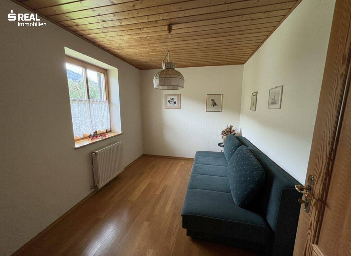 Kleineres Schlafzimmer mit Holzboden, Sofa und Fenster mit Blick nach draußen.