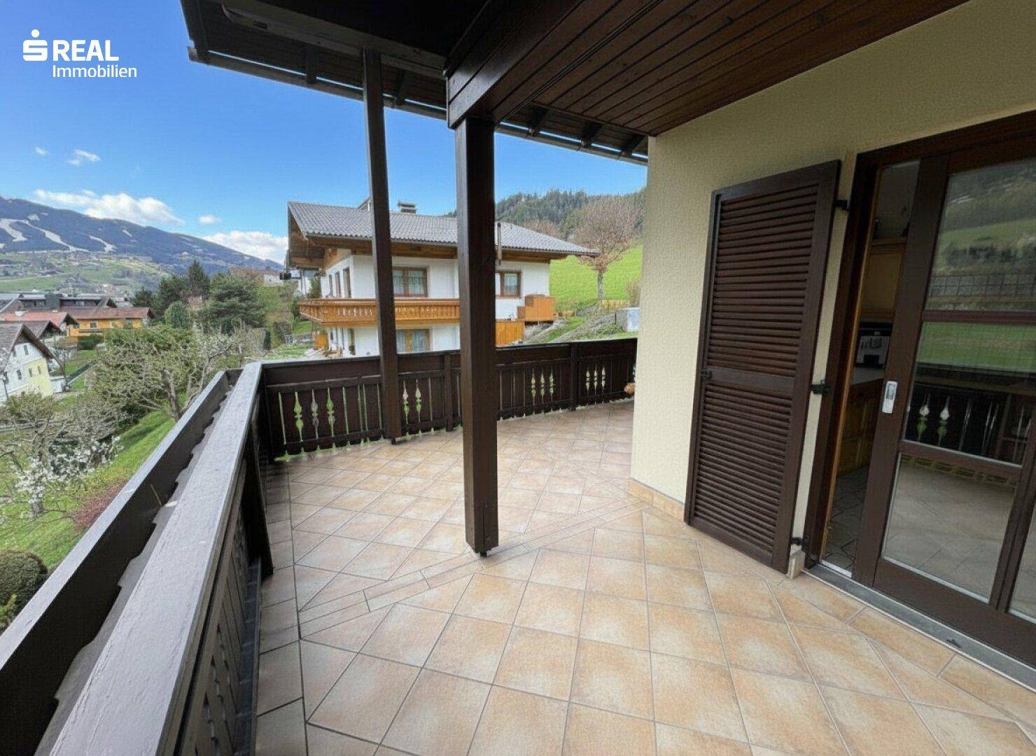 Überdachter Balkon mit Fliesenboden und Zugang zum Innenbereich des Hauses.