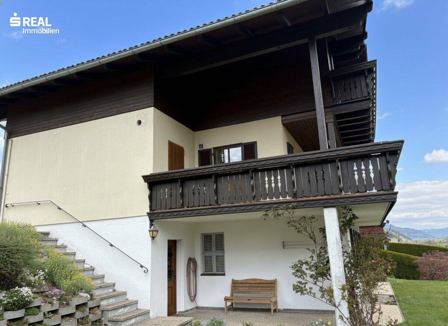 Seitenansicht des Hauses mit Balkon, Außentreppe und Blick auf die umliegende Landschaft.