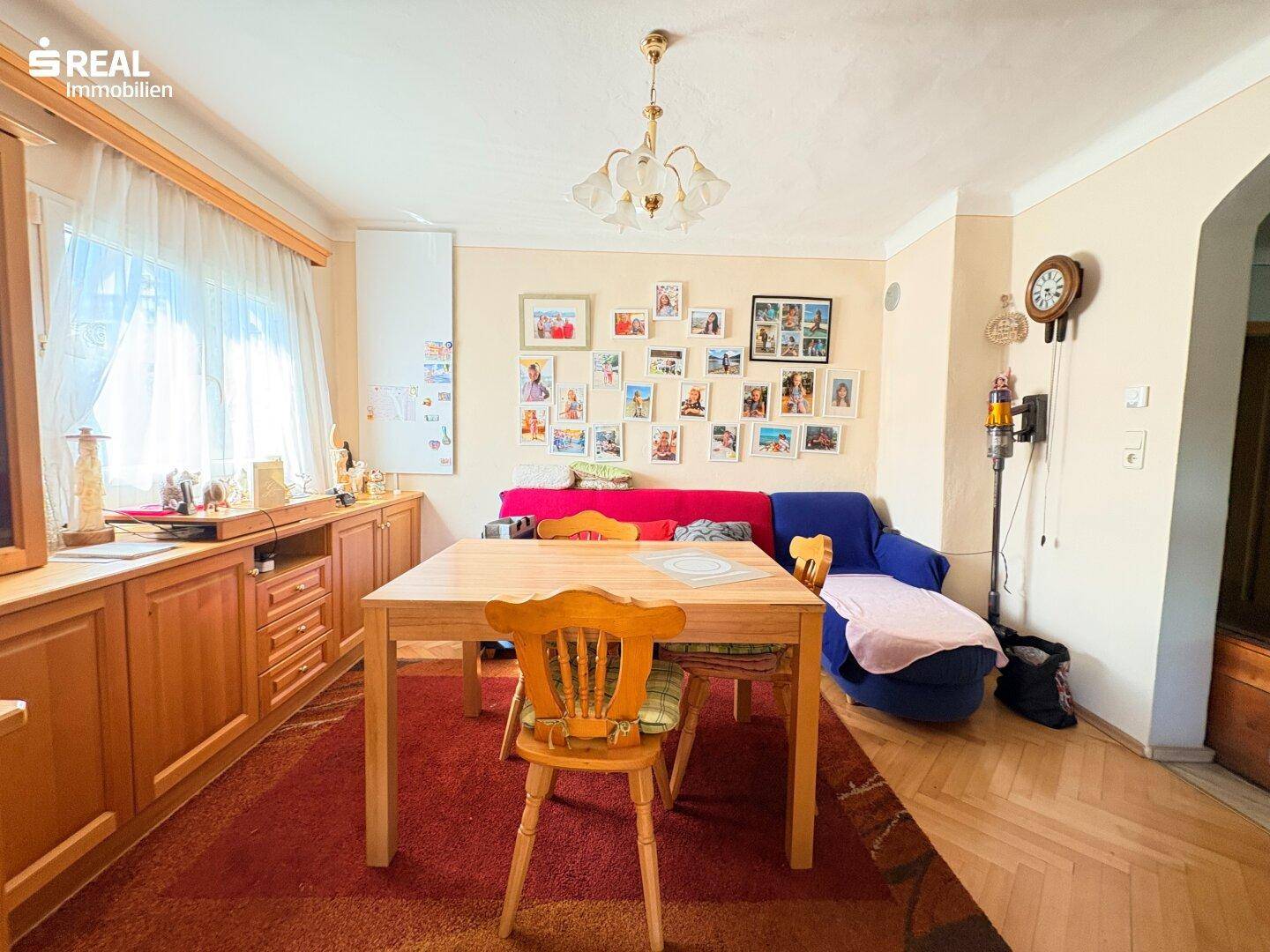 Gemütlicher Essbereich mit Holztisch, Teppichboden und Sofa, dekoriert mit Familienfotos.