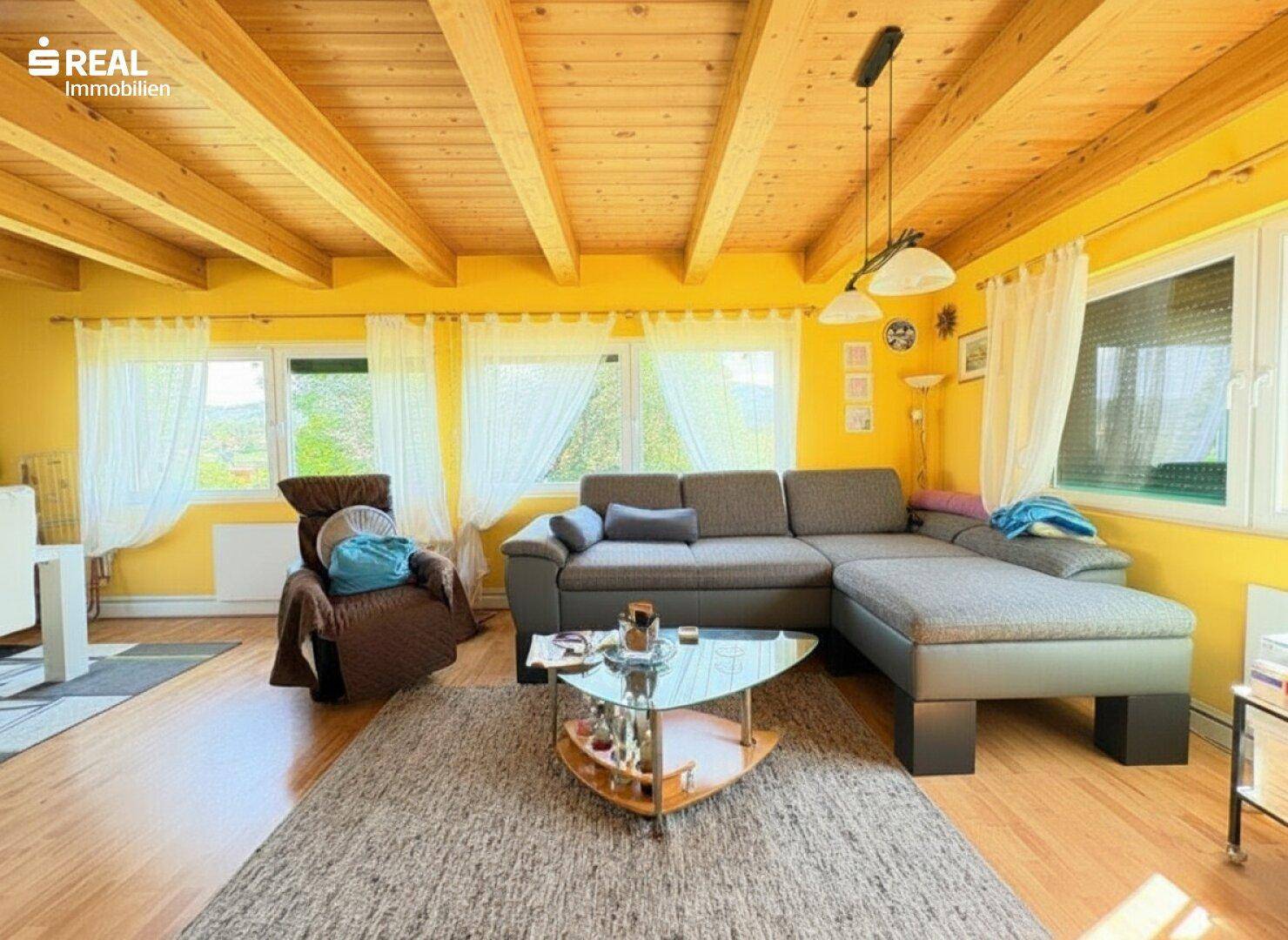 Geräumiges Wohnzimmer mit Holzbalkendecke, gelben Wänden und bequemer Sofalandschaft.