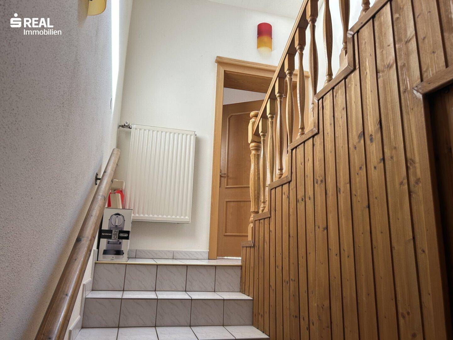 Holztreppe mit gefliesten Stufen und Holzvertäfelung, die in die obere Etage führt.