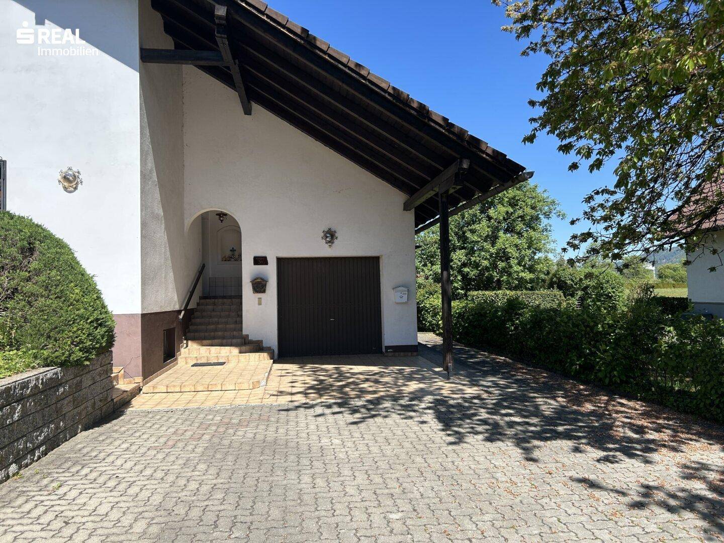 Eingangsbereich des Hauses mit Treppe und integrierter Garage, umgeben von gepflasterter Fläche.