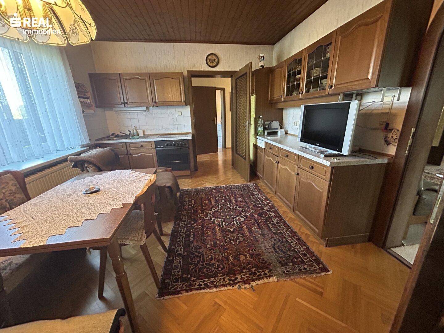 Traditionelle Küche mit Holzschränken, Essbereich und Blick auf den Garten durch das Fenster.