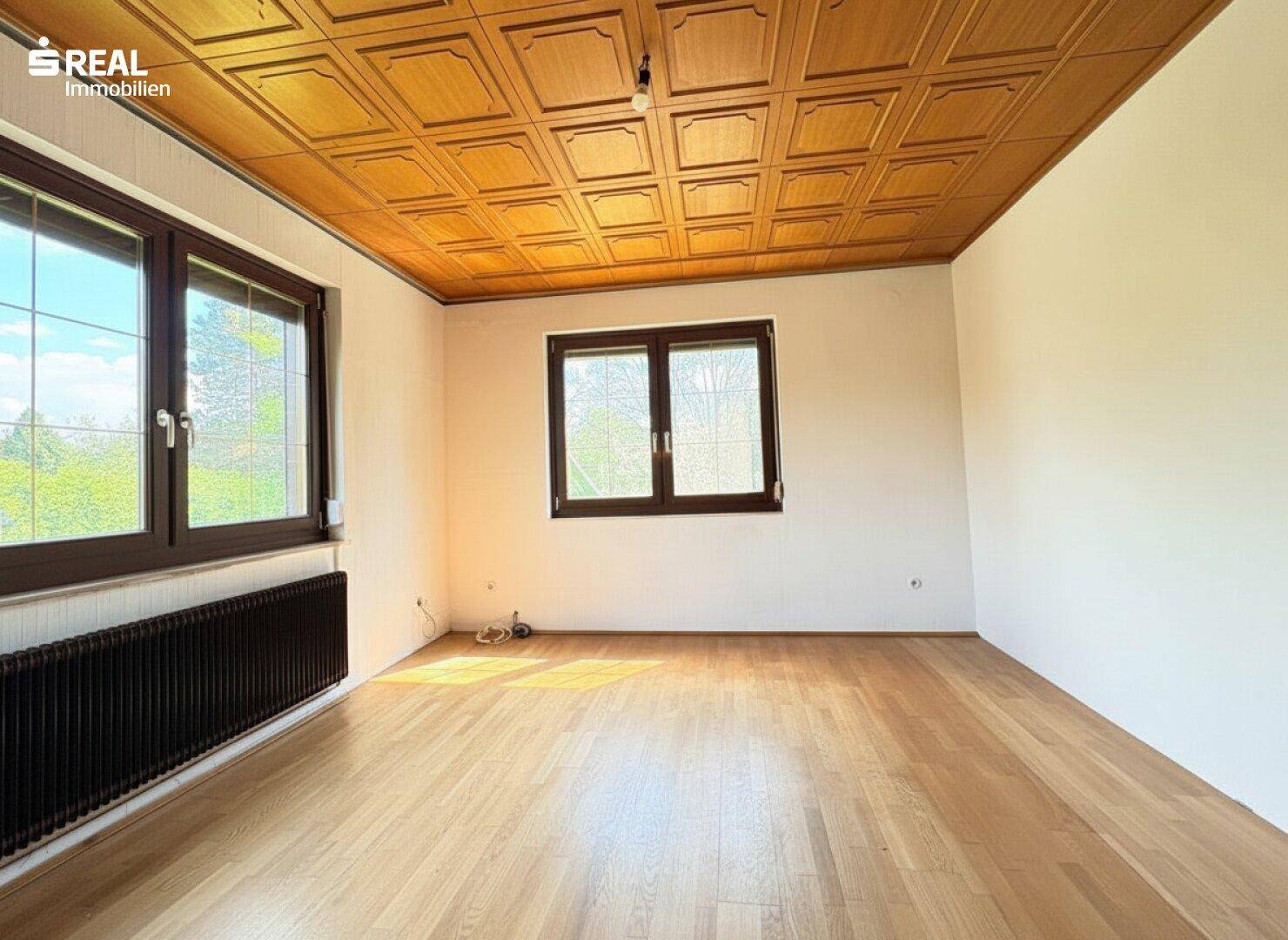 Geräumiges Zimmer mit Holzkassettendecke, Parkettboden und großen Fenstern.