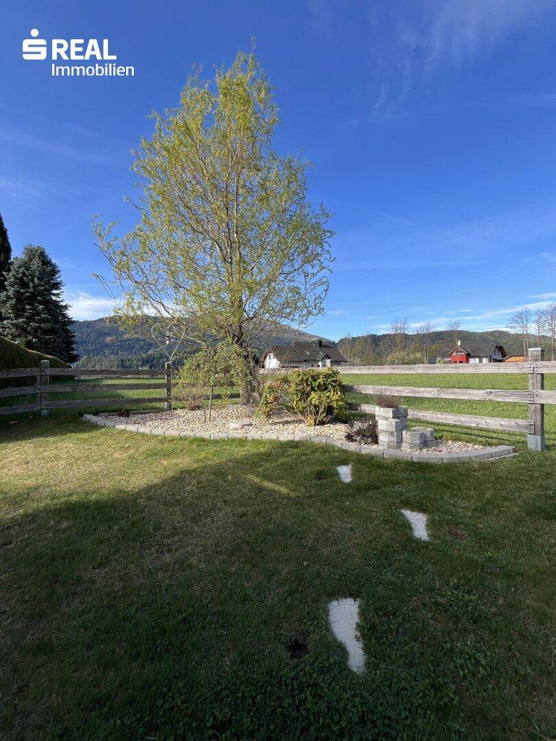 Gepflegter Gartenbereich mit jungem Baum und Holzzaun, umgeben von grüner Wiese.