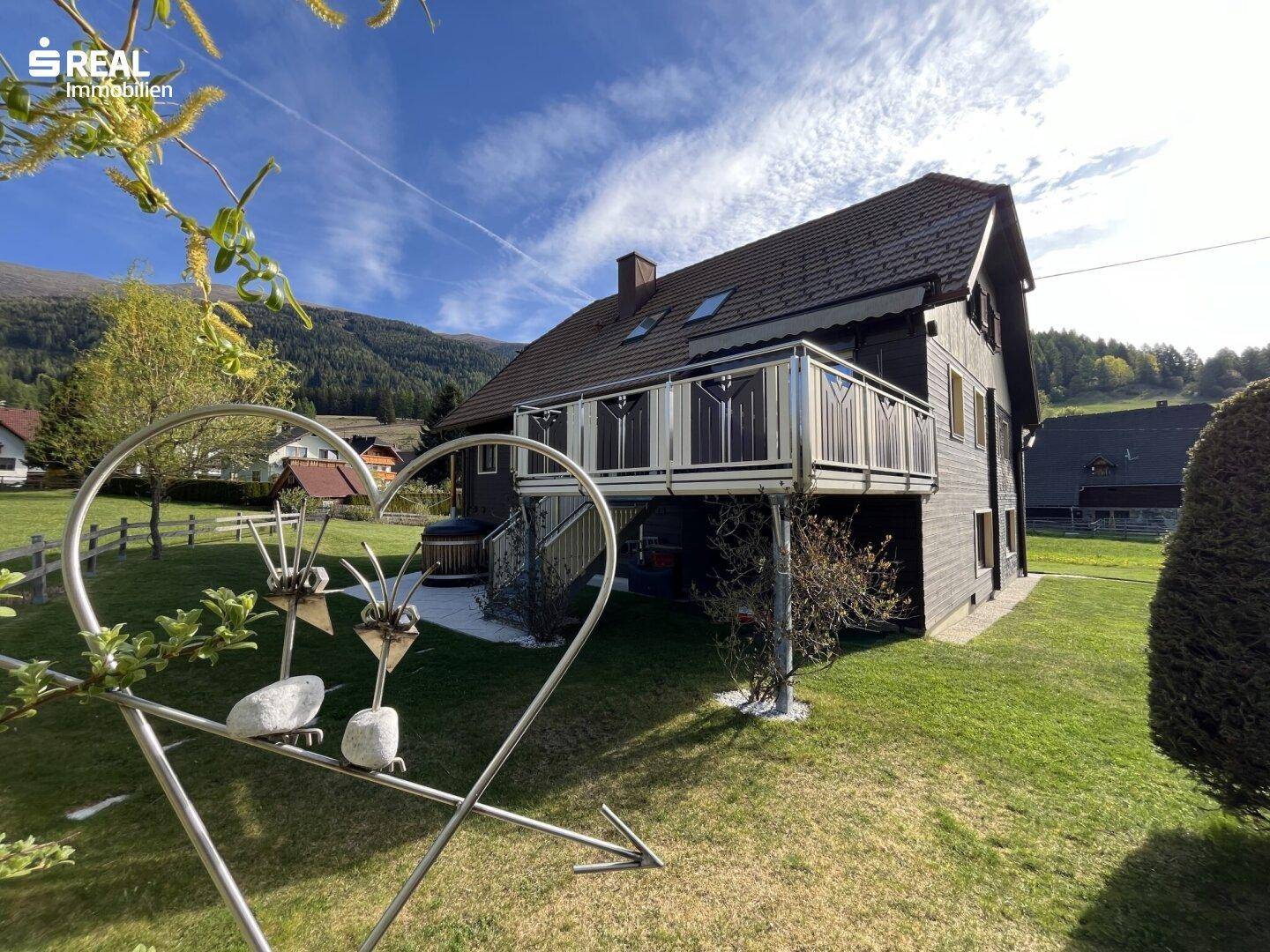 Seitenansicht des Hauses mit Balkon, Whirlpool und dekorativer Gartenskulptur im Vordergrund.