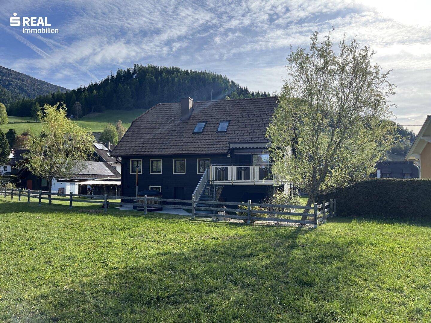 Rückansicht des Hauses mit Balkon, Dachfenstern und Blick auf die umliegende Berglandschaft.