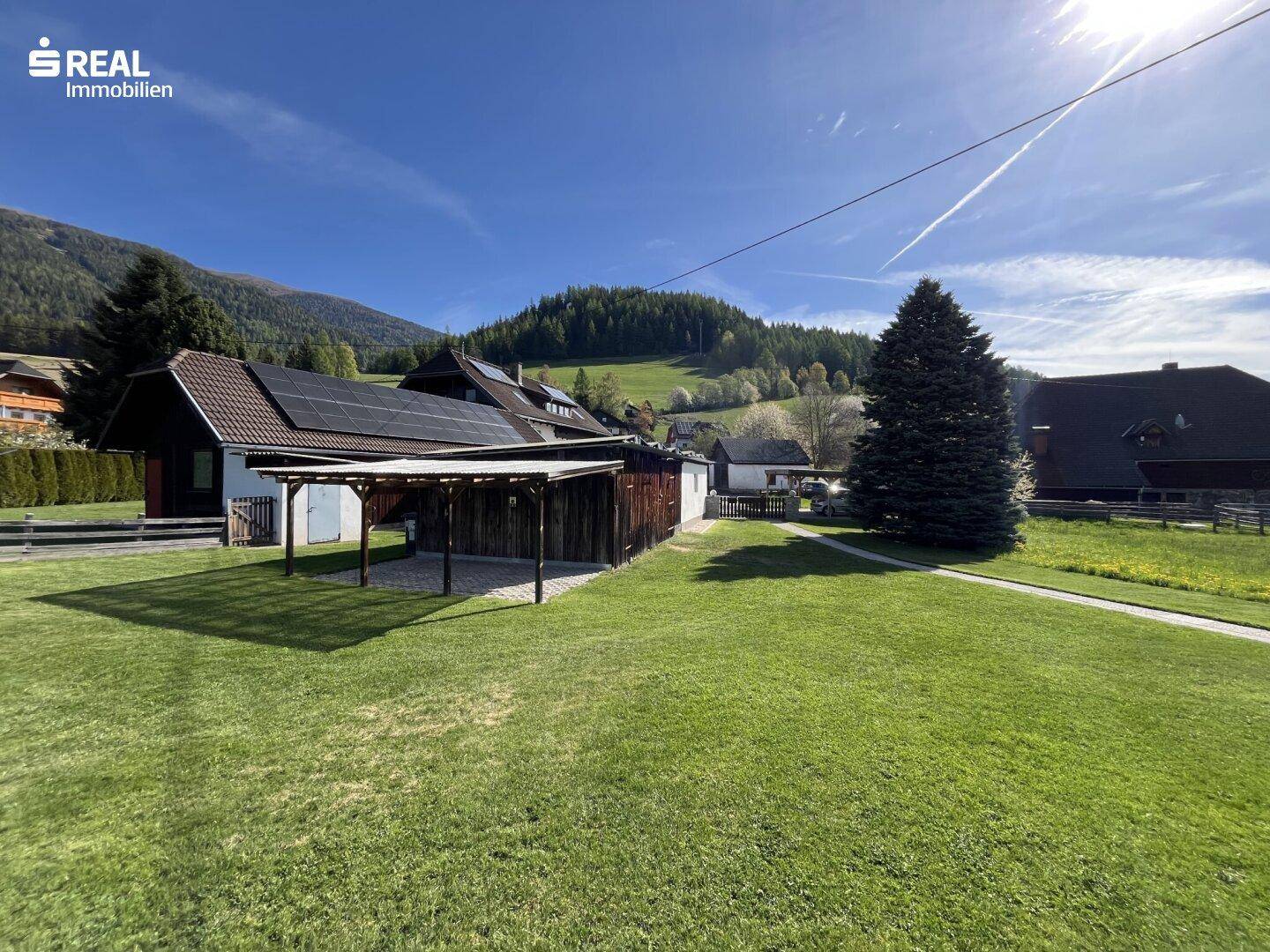 Geräumiger Gartenbereich mit Carport und Blick auf die bewaldeten Hügel und Berge.