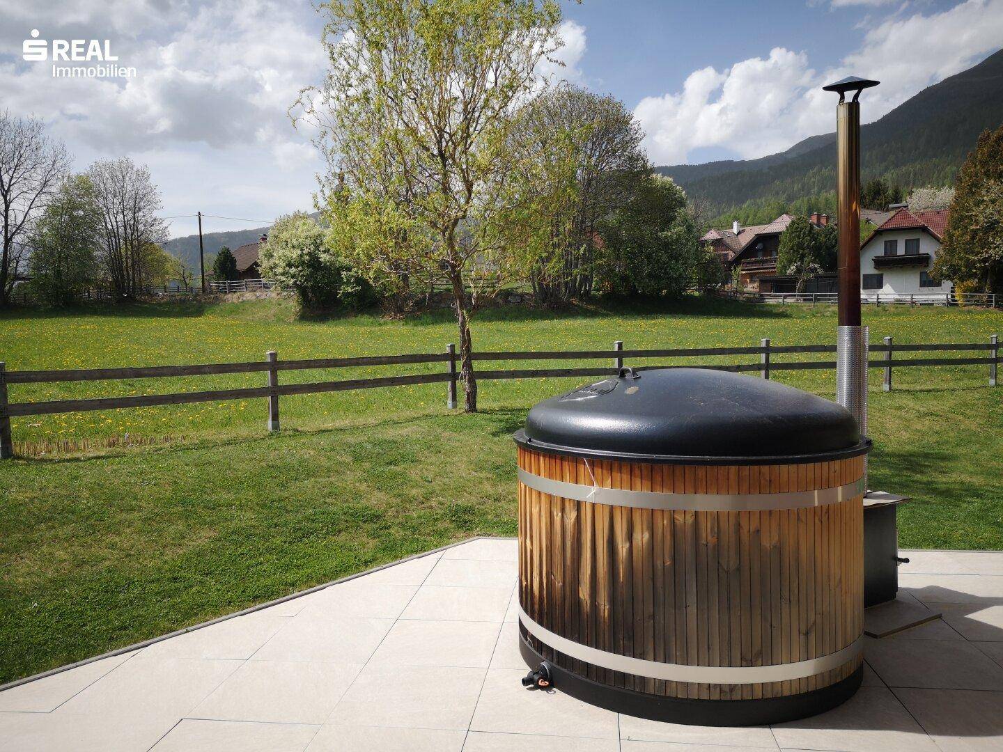 Gemütliche Terrasse mit Holz-Whirlpool und weitem Blick über die grüne Landschaft.