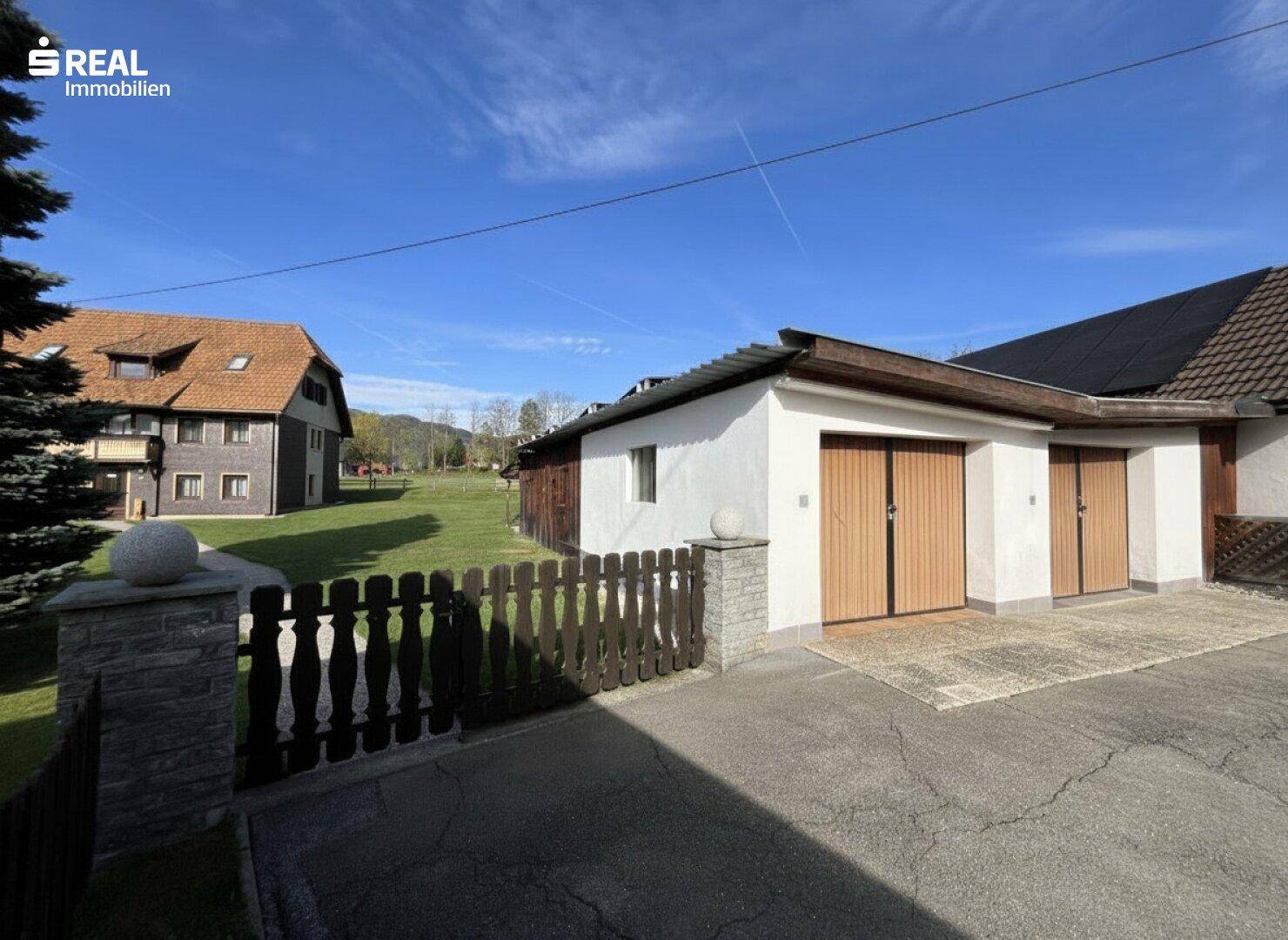 Doppelgarage mit Holztoren und gepflasterter Zufahrt, im Hintergrund das Haupthaus.