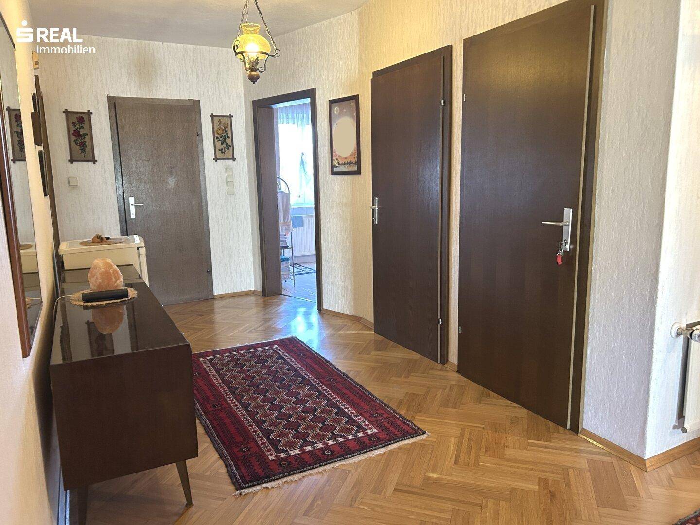 Heller Flur mit Fischgrätparkett, dunklen Türen und traditionellem Teppichläufer.