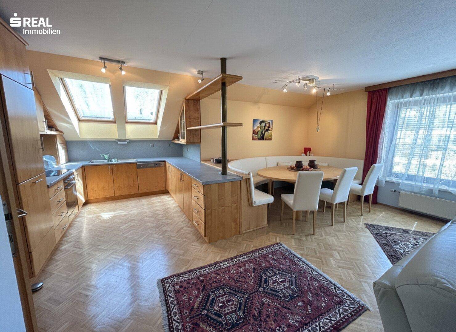 Geräumige Dachgeschossküche mit Essbereich, Holzmöbeln und viel Tageslicht durch die Dachfenster.