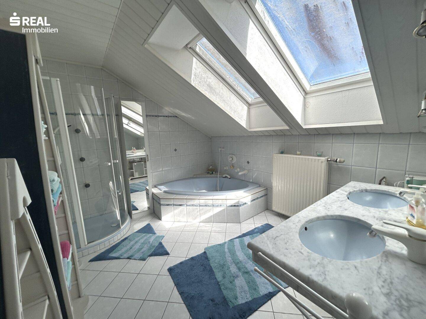 Helles Dachgeschossbad mit Eckbadewanne, Dusche, Doppelwaschbecken und Dachfenstern.