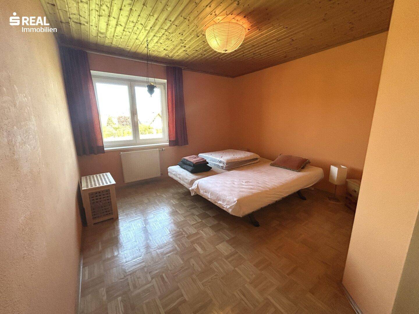 Schlafzimmer mit Holzbalkendecke, Parkettboden und zwei Einzelbetten.